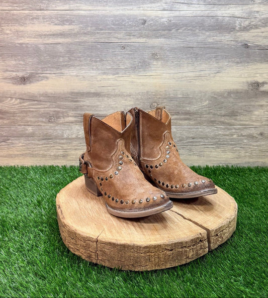 Pair of brown ankle studded cowboy boots with studs on a wooden platform against a wooden wall.