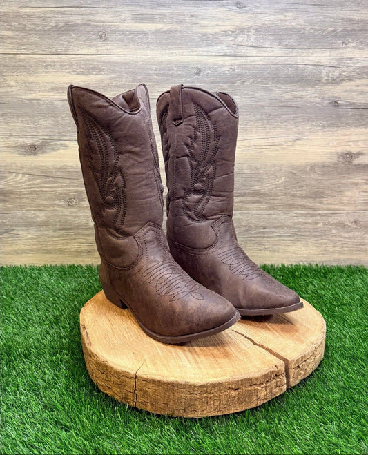 Pair of brown cowboy boots on a wooden block with a grass and wood panel background