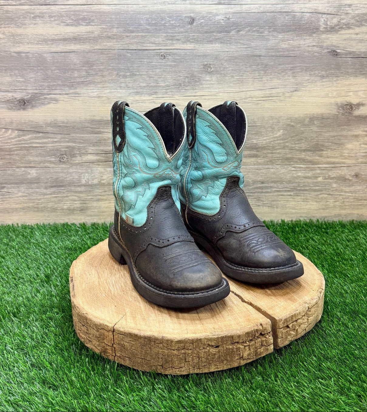 Pair of black cowboy boots with turquoise design on a wooden platform